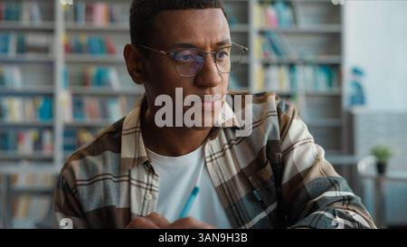 Tired sleepy bored African American man yawning male student laptop write notepad lesson online learning studying university library high school Stock Photo