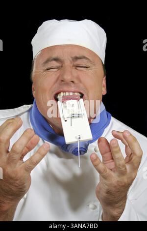 Chef in pain with mousetrap caught on his tongue Stock Photo