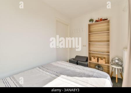 A serene and tidy bedroom featuring a neatly made bed, wooden shelf, and simple decor, showcasing a minimalist design aesthetic that promotes tranquility. Stock Photo