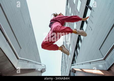 Young woman dancer in pink sport outfit jumping very high with bended knees and arms raised, low angle view Stock Photo