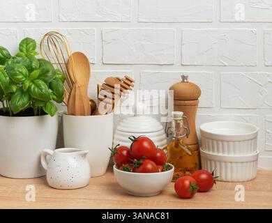Modern kitchen counter displaying fresh ingredients, wooden utensils, and white ceramic tableware, creating a stylish and inviting culinary setting Stock Photo