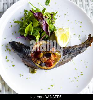 Baked trout with vegetables served in large white dish with arugula leaves, young beetroot and slice of lemon. Healthy and tasty food. Close-up. Top v Stock Photo