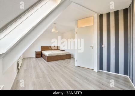 A spacious modern bedroom featuring a minimalist design with a wooden bed frame, light wooden flooring, and striped wallpaper, creating a bright, airy atmosphere. Stock Photo