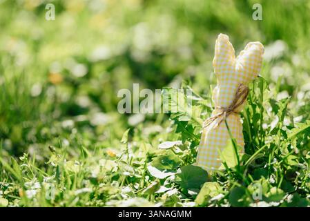 Handmade fabric Easter bunnies in yellow and green placed on vibrant green grass under bright spring sunlight Stock Photo