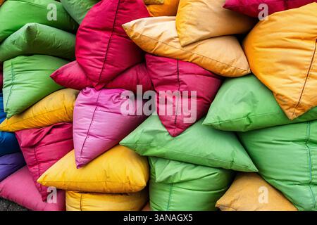 Pile of colorful beanbags and pillows stacked on top of each other. The pillows are of different colors and sizes, creating a vibrant and lively atmos Stock Photo