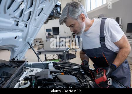 Man mechanic checking car battery using voltmeter in repair service Stock Photo