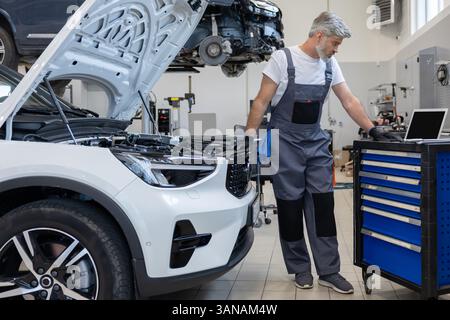 Engineer bearded man looking at inspection vehicle details under car hood using laptop Stock Photo