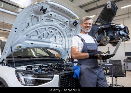 Mechanic in garage working on car maintenance using laptop for engine inspection Stock Photo
