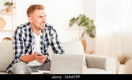 Portrait of man sitting on sofa using phone and pc Stock Photo