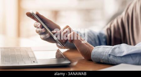 Female hands holding smartphone and using laptop Stock Photo