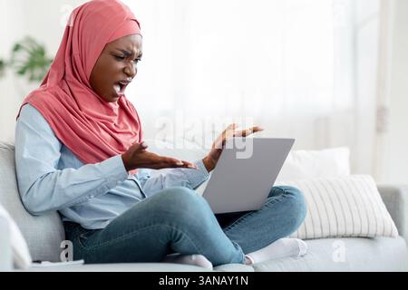 Computer Problems. Angry black muslim lady having troubles with laptop at home Stock Photo