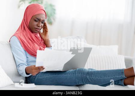 Black Muslim Lady Having Headache While Working Remotely With Papers At Home Stock Photo
