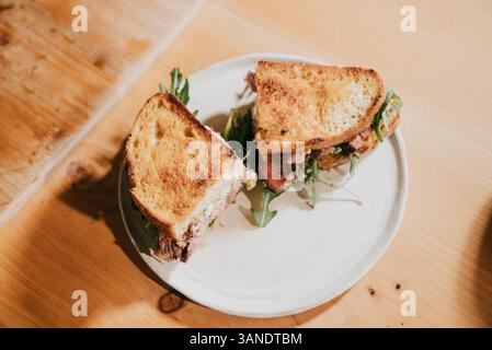 A sandwich is cut in half and placed on a white plate. The sandwich is made with meat and greens Stock Photo