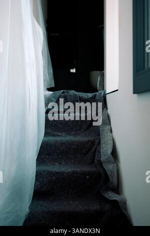 Indoor staircase covered with fabric and plastic sheets, showing a home under renovation. Stock Photo