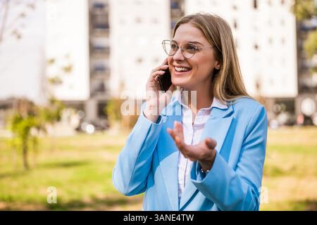 Successful female entrepreneur confidently discussing business details on her mobile phone in city park. Stock Photo
