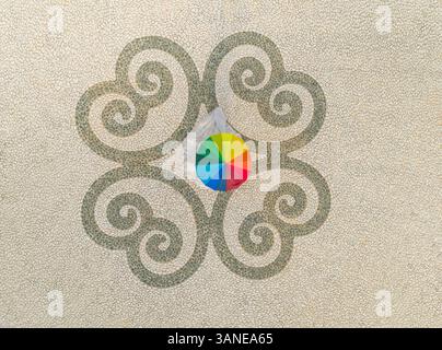 Aerial view of woman in wedding dress holding rainbow umbrella on pebble background on Santorini island, Mesaria, Greece. Stock Photo