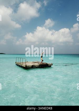 Aerial view of man doing a handstand on a Pontoon in the crystal clear blue turquoise ocean in the tropical paradise Maldives, Indian Ocean. Stock Photo
