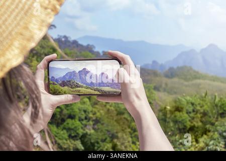 a female traveler photographing nature on her phone - mountains and rainforests in Thailand. Hands and phone close-up rear view. The concept is a pass Stock Photo
