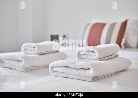 Close up of freshly folded white towels placed on neatly made bed in modern, minimalistic bedroom Stock Photo