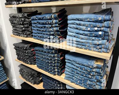 Stacked denim jeans in different shades - black, dark blue and light blue - on wooden shelves in retail clothing store. Stock Photo