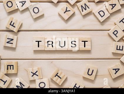 Wooden board with a word written in black letters on it. The word is "trust," and it is surrounded by wooden blocks that spell out the word. The block Stock Photo