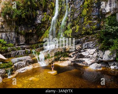 Aerial view of a woman standing in front of a waterfall in black swimsuit, Rawsonville, Western Cape, South Africa. Stock Photo