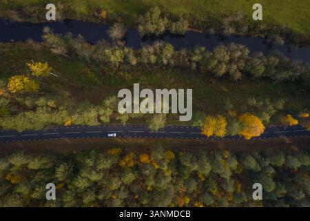 Aerial view above of river crossing forest near an empty road, Estonia. Stock Photo