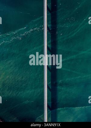 Aerial view of a straight road going over the beautiful blue Atlantic Ocean, surrounded by tiny ice shards in Eyrarbakki, South Iceland Stock Photo