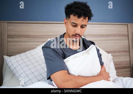 Young Man in a Contemplative Mood Sitting in Bed During Morning Stock Photo