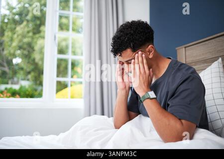 Man Sitting in Bed at Home Holding Head, Experiencing Discomfort Stock Photo