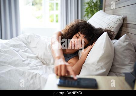 Young Woman Lying in Bed Interacting with Her Phone, Morning Routine Scene Stock Photo
