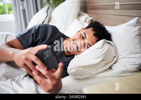 Young Man Relaxing in Bed and Using Smartphone at Home in the Morning Stock Photo
