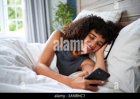 Young Woman Relaxing in Bed and Enjoying Her Digital Device in a Serene Atmosphere Stock Photo