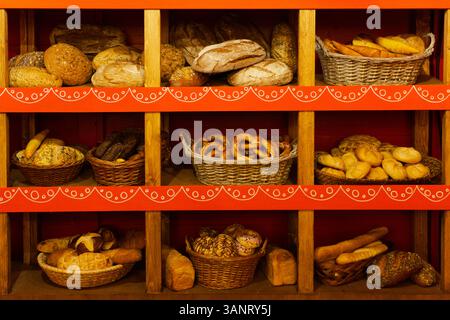 The image displays a variety of freshly baked bread and pastries on wooden shelves in a cozy bakery. Stock Photo