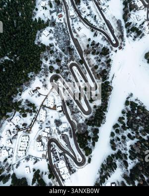 Aerial view of a zigzag road winding through a dense green forest with ...