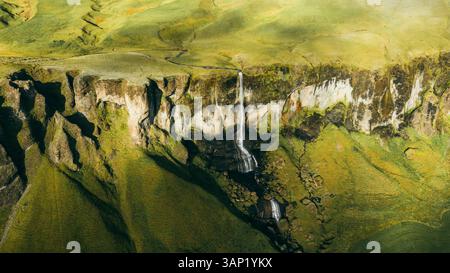 Aerial view of the majestic Foss a Sidu waterfall cascading over a rocky cliff in a lush green valley, Skaftarhreppur, Iceland. Stock Photo