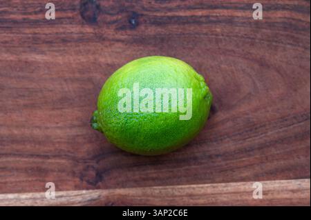 A whole green lime on a wood cutting board Stock Photo