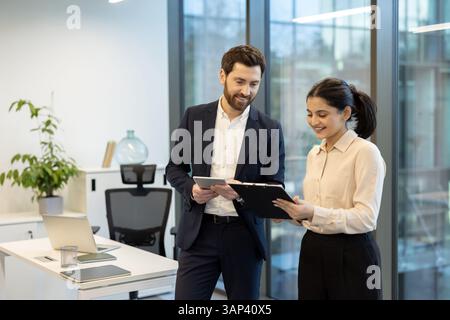 A diverse team of professionals collaborates in a modern office environment, reviewing documents and using a tablet together, creating a focused work atmosphere. Stock Photo