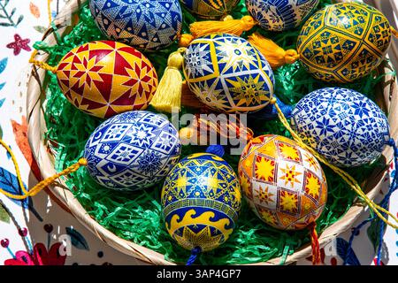 A vibrant collection of traditional Ukrainian pysanky is beautifully arranged in a basket filled with green grass. Stock Photo