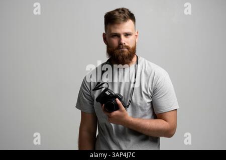 Portrait of bearded professional photographer with photo camera looks straight into the camera. Stock Photo