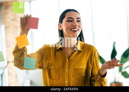 Qualified professional young woman engaging in a teamwork session using colorful notes in a luminous and modern office environment Stock Photo