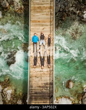 Aerial view of sporty family lying on wooden suspension bridge above a river. Stock Photo