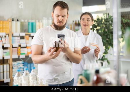 Attentive man scans QR code on box cough syrup label. Female pharmacist offers various cough syrups Stock Photo