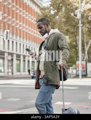 African American man using a smartphone while standing on the European city street with modern and historic architecture buildings. Stock Photo