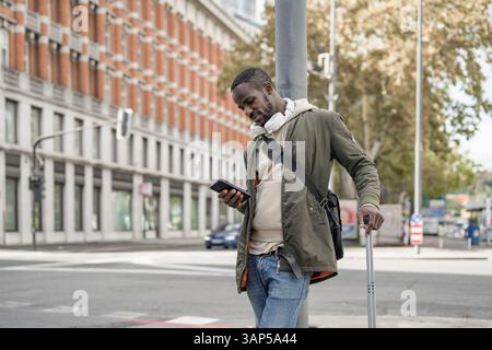 African American man using a smartphone while standing on the European city street with modern and historic architecture buildings. Stock Photo