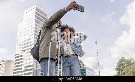 African American tourist couple having fun taking selfies on a busy European city street with modern skyscraper architecture. Stock Photo