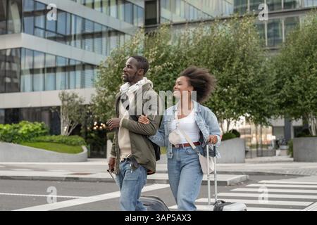 Loving African American couple, tourists with luggage walking city streets holding hands and watching the urban environment. Stock Photo