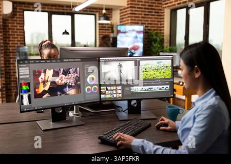 Skilled female video specialist edits raw content, applies motion graphics, and ensures high quality results in office. Asian woman seated with multiple screens, focused on adjusting cinematic visuals Stock Photo