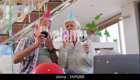 Happy caucasian senior couple in party hats making birthday laptop image call drinking wine Stock Photo