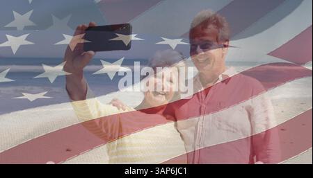 Image of happy senior caucasian couple taking selfies over flag of united states of america Stock Photo